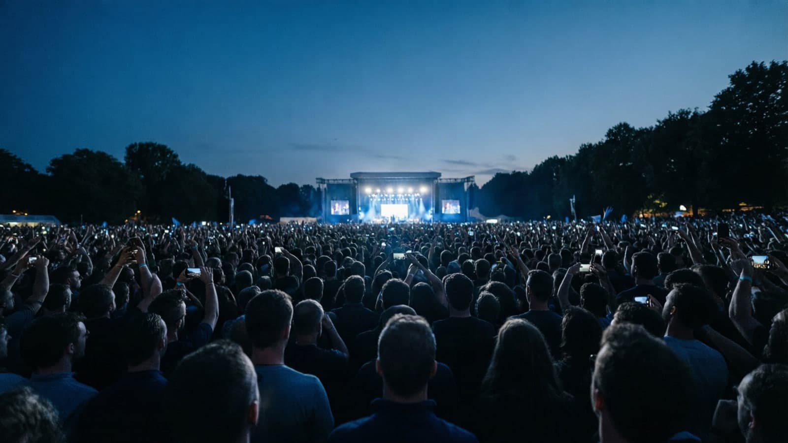 A large crowd at an outdoor rally at dusk, seen from behind the crowd